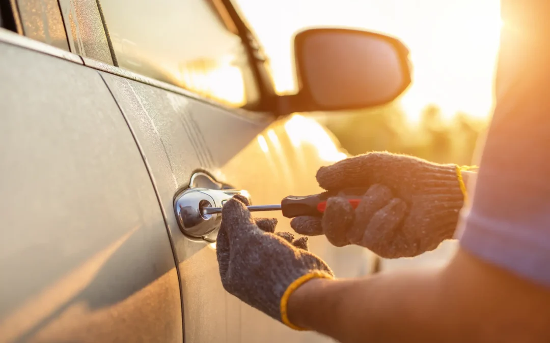 Close-up of car door lock being picked with screwdriver by man wearing gray gloves against sun-drenched background