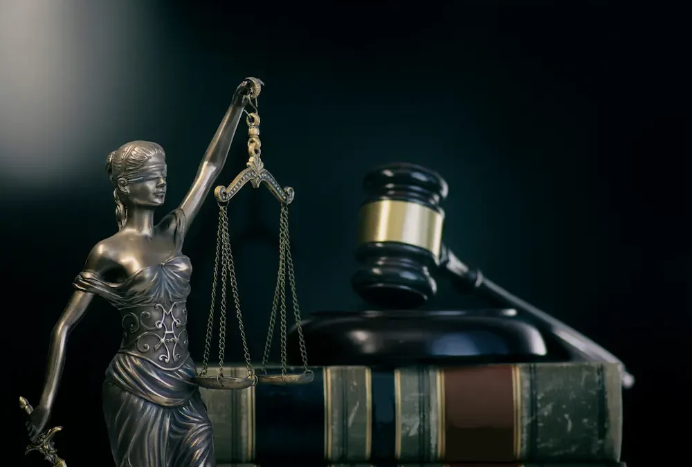 Small bronze statue of Lady Justice in front of black gavel on legal book