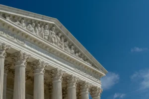 West façade of United States Supreme Court building in front of blue sky. The Neoclassical federal courthouse features carved figures and the motto "Equal Justice Under Law" above marble columns.